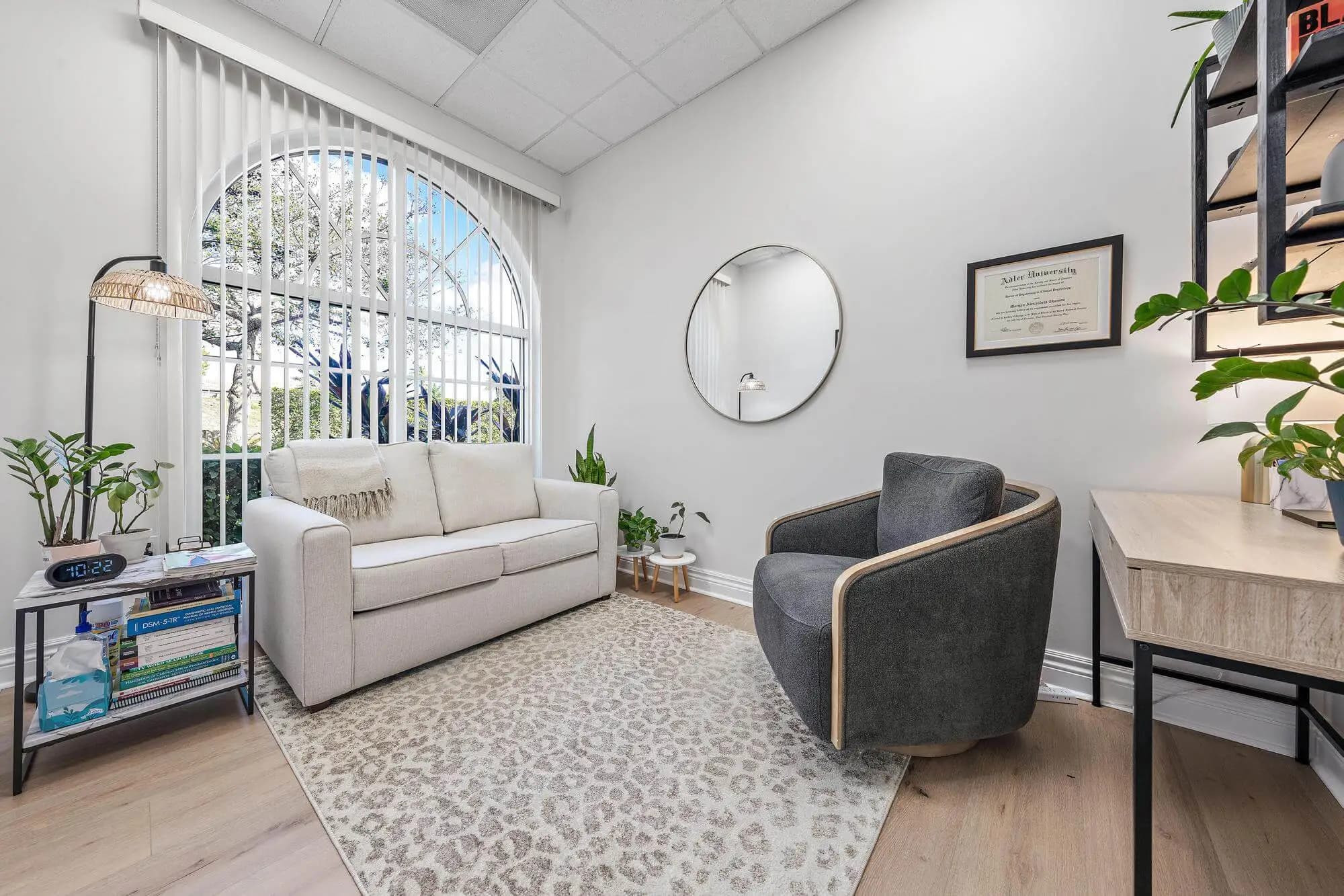 Therapy room with cream sofa, swivel chair, and arched window