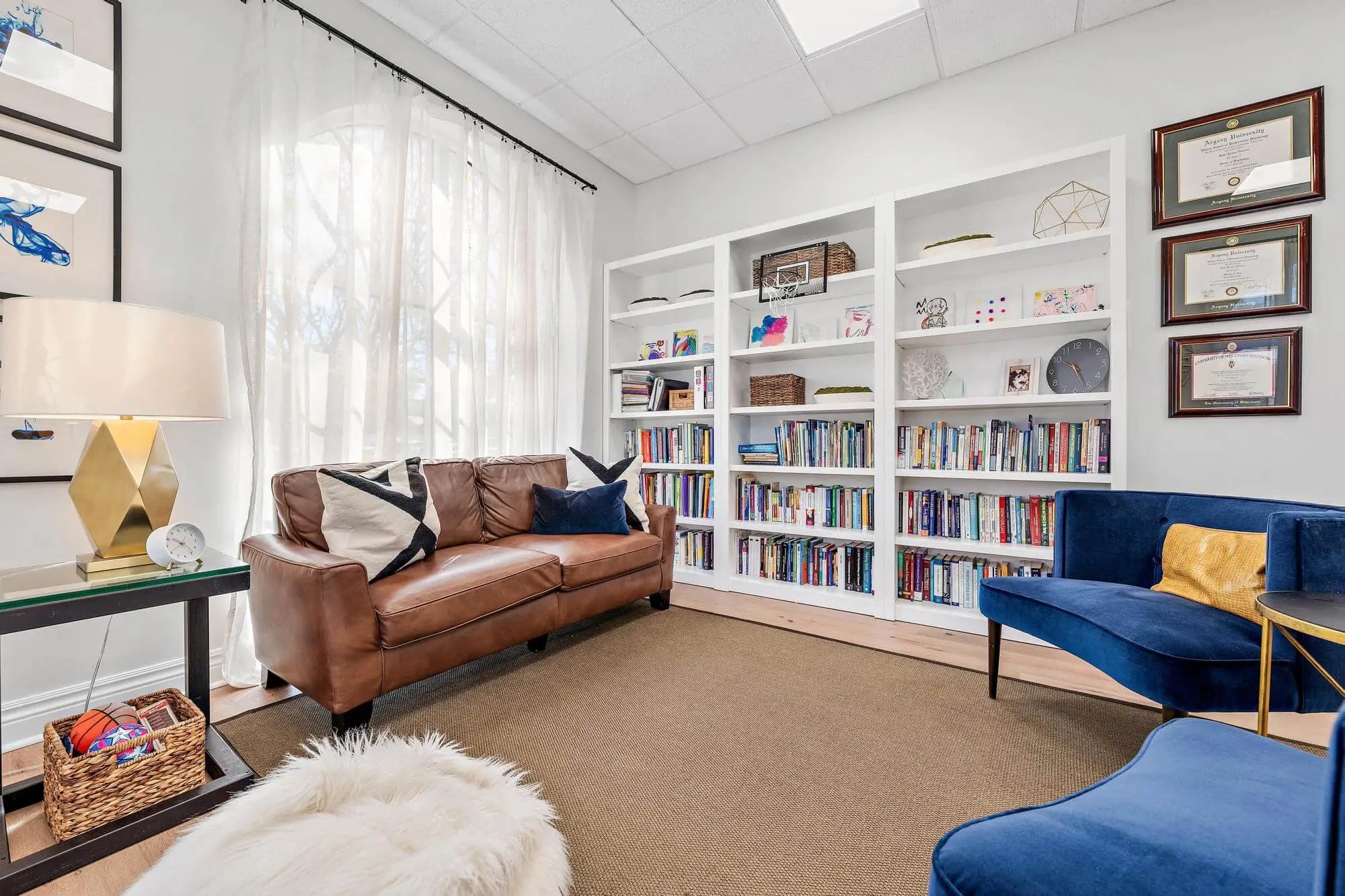 Therapy room with leather sofa, blue accent chairs, and floor-to-ceiling bookshelves